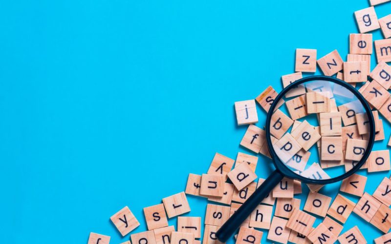 Decoding Diamond Painting blog post header: Wooden Scrabble board game letter tiles and magnifying glass on bright blue background