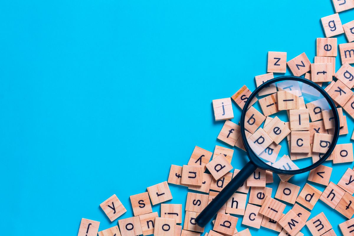 Decoding Diamond Painting blog post header: Wooden Scrabble board game letter tiles and magnifying glass on bright blue background