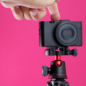 About creators: Digital camera on a tripod with hand pressing record button